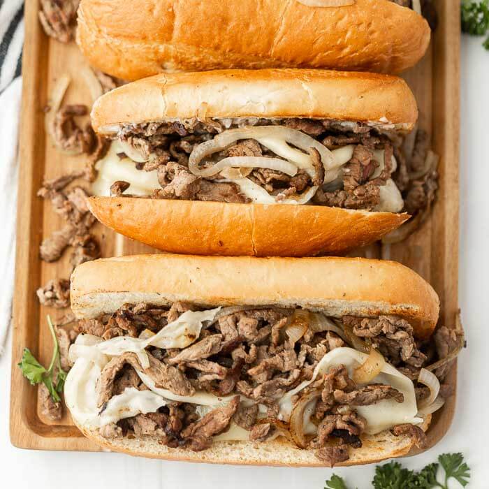 Philly Cheesesteaks lined up on a baking sheet. 