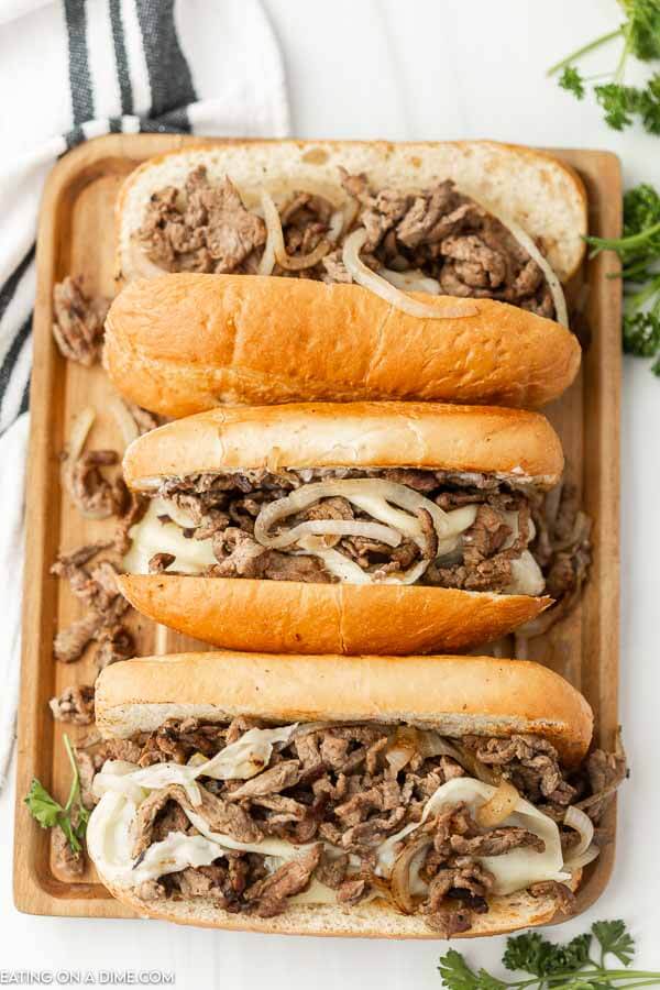 Philly Cheesesteaks lined up on a baking sheet. 