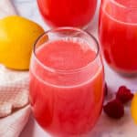 Raspberry lemonade in a glass with lemons and raspberries.