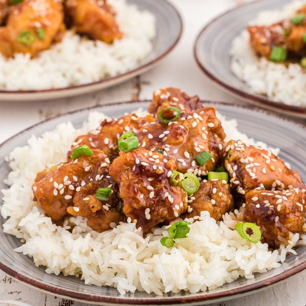 Close up image of sesame chicken on rice on a plate