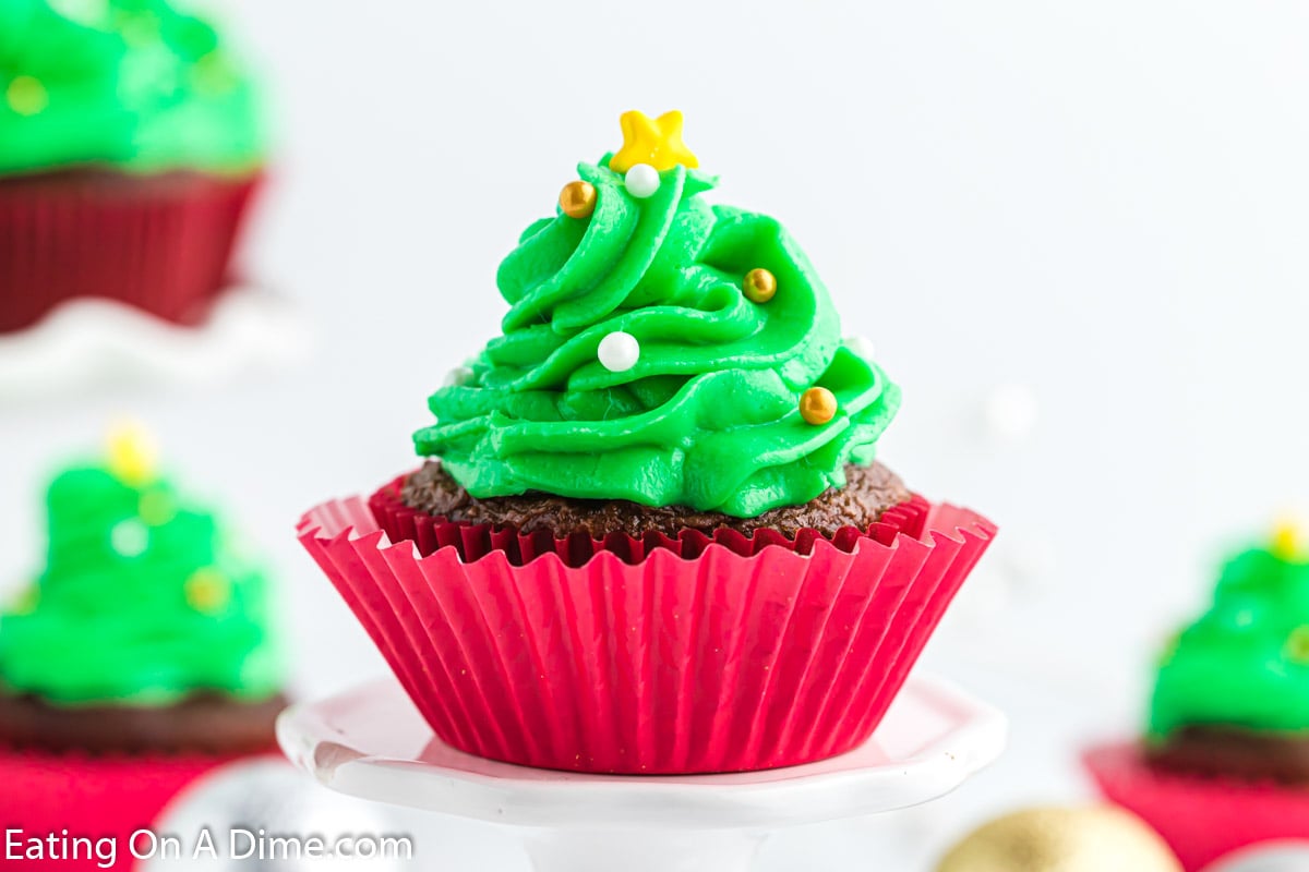 Cupcake topped with green frosting in a shape of a Christmas Tree topped with yellow sprinkle star and candy balls