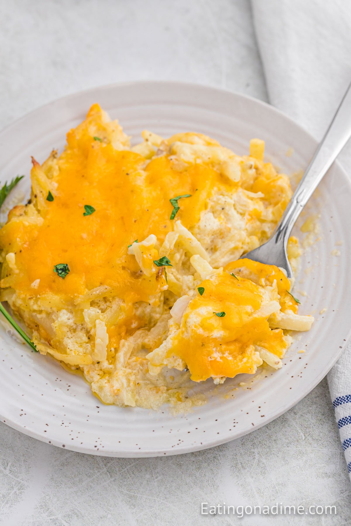 cheesy hashbrown casserole on a white plate with a serving on a fork