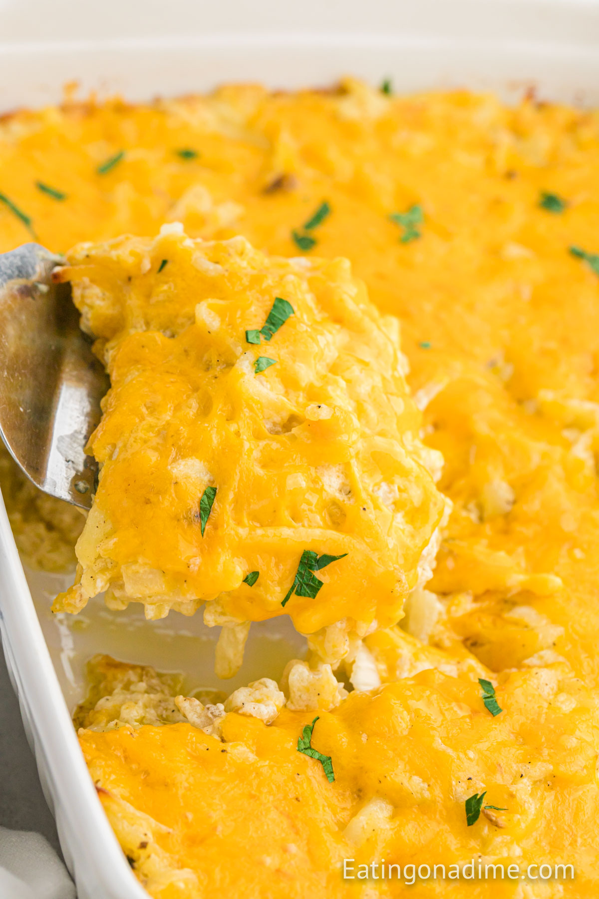 Cheesy Hashbrown Casserole in a baking dish with a serving on a spatula
