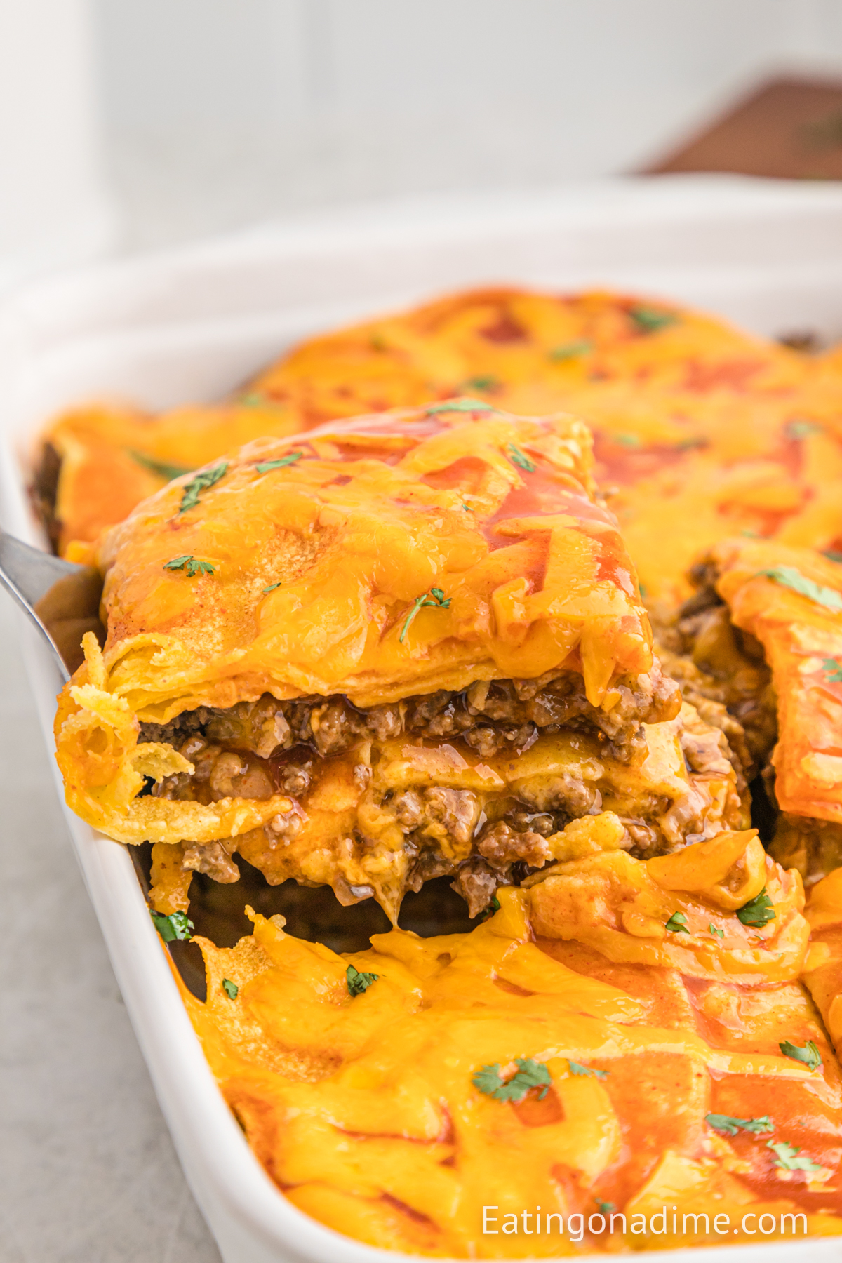Close up image of beef enchilada casserole in a baking dish with a serving on a spatula