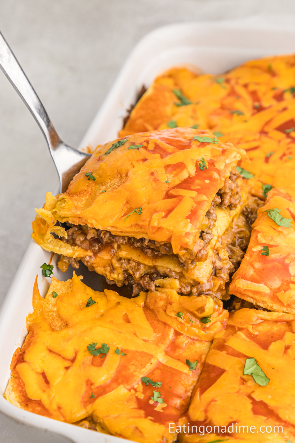 Close up image of beef enchilada casserole in a baking dish with a serving on a spatula