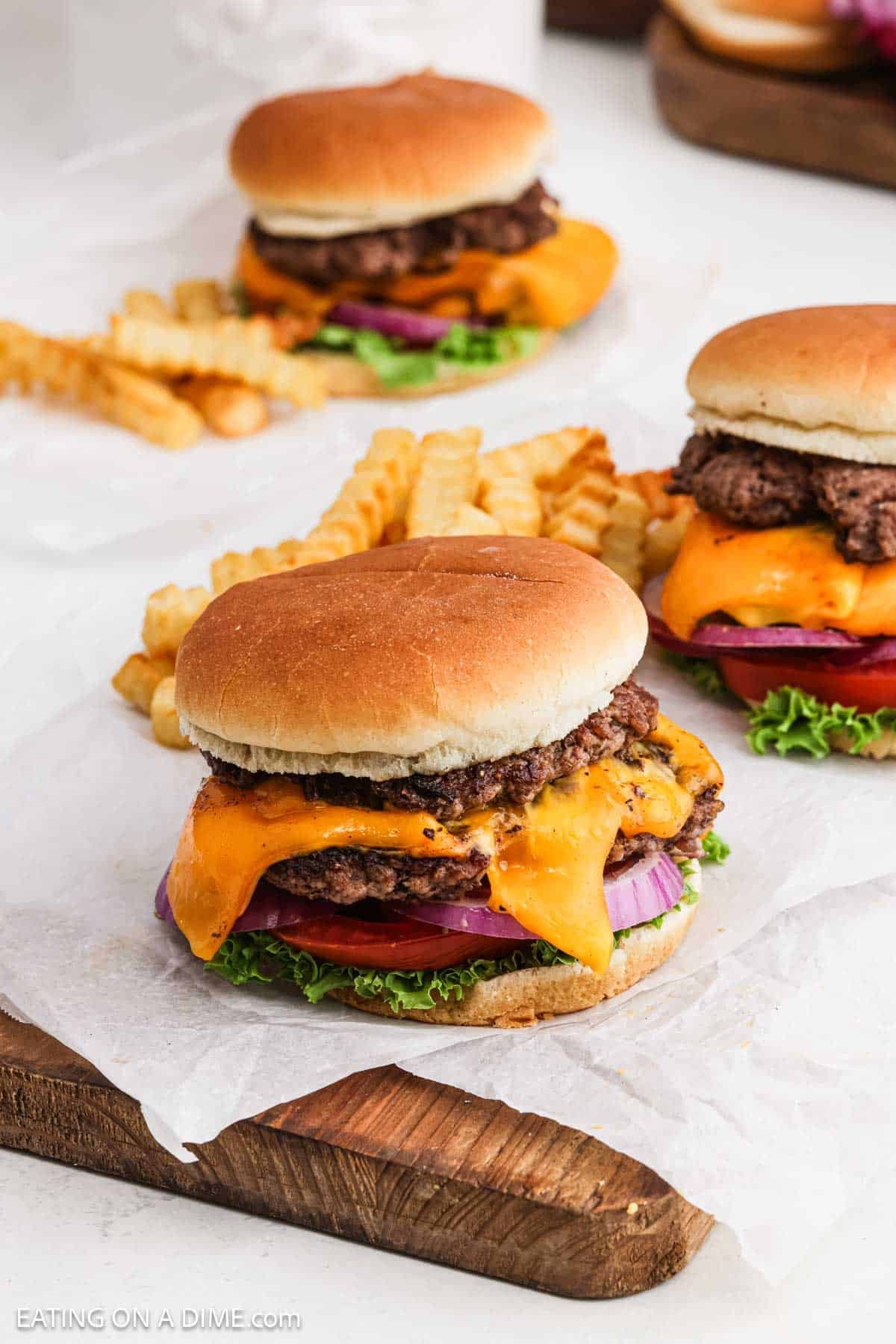 Cheeseburgers topped with sliced red onions, tomatoes and lettuce with french fries in the background.