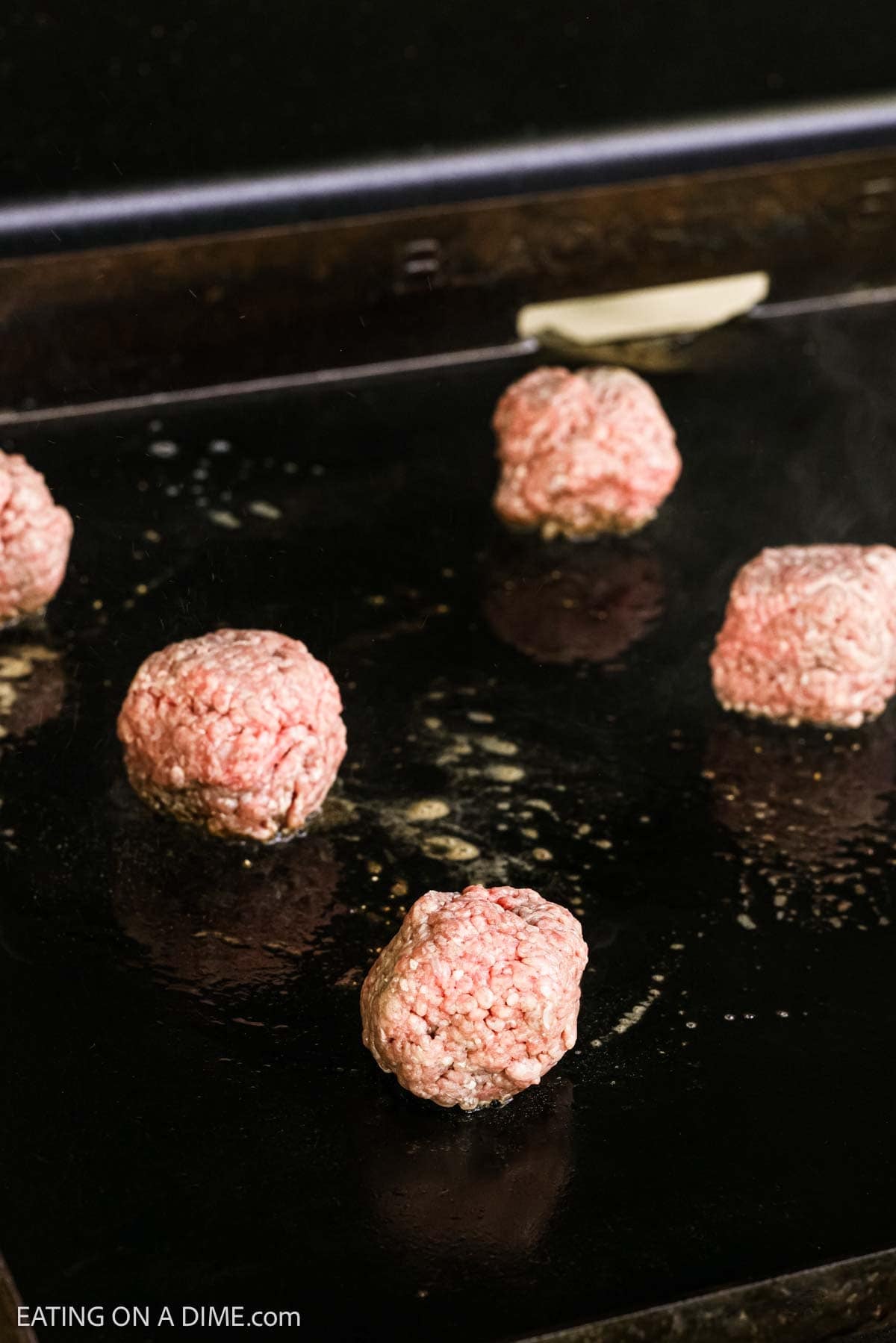 Placing the hamburger balls on the flat top griddle.
