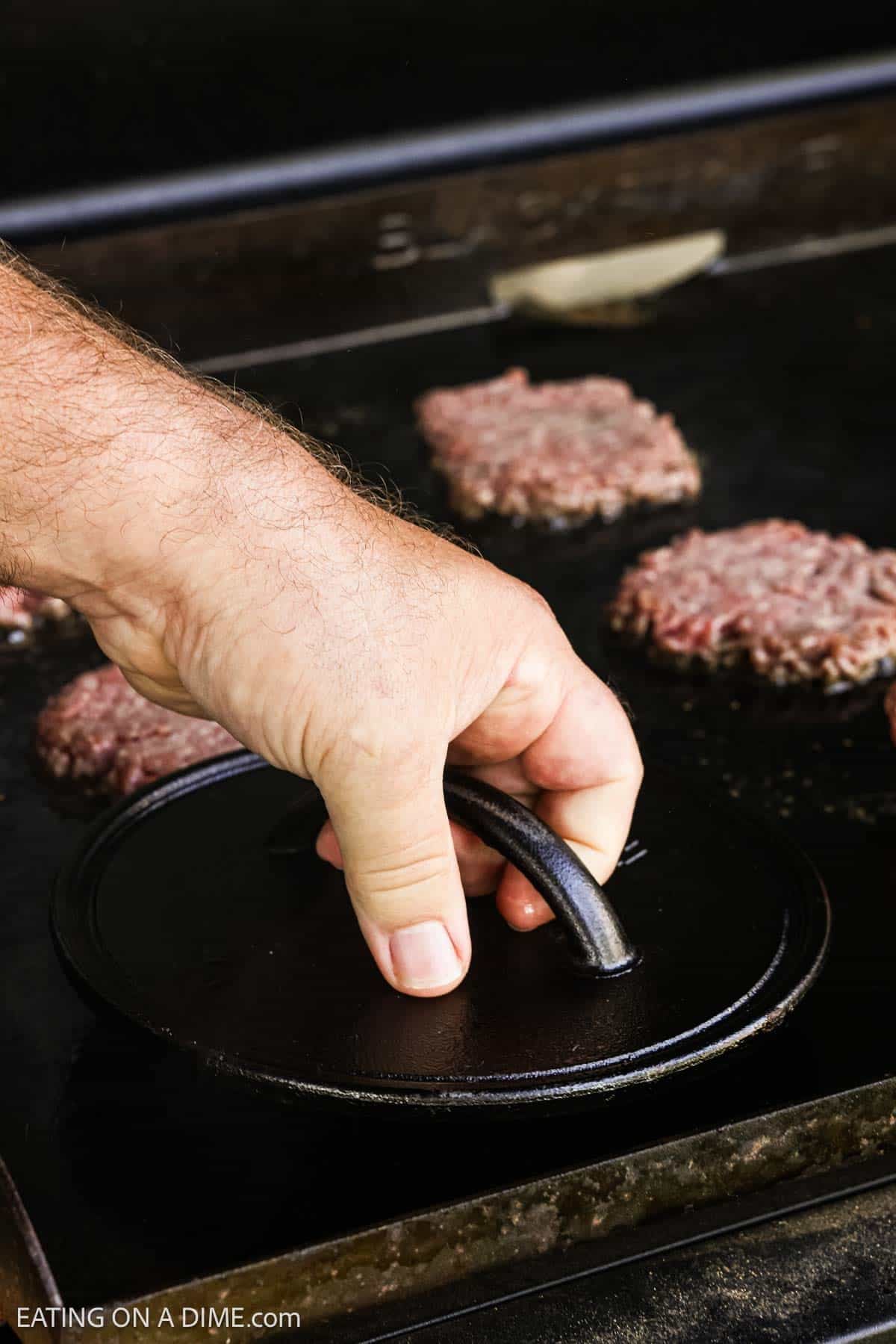 Smashing the hamburger patties with a burger press on the flat top griddle.