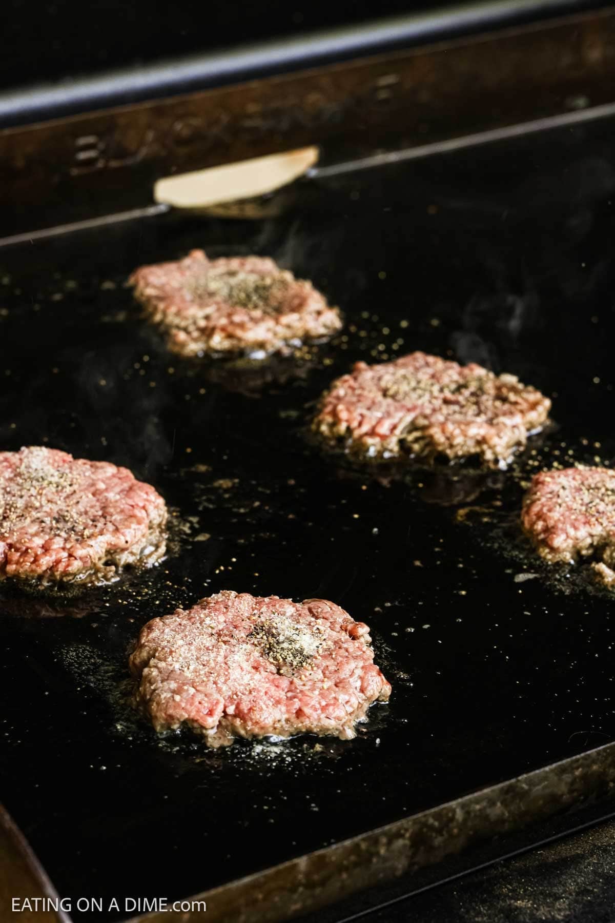 Seasoned hamburger patties on the flat top griddle.