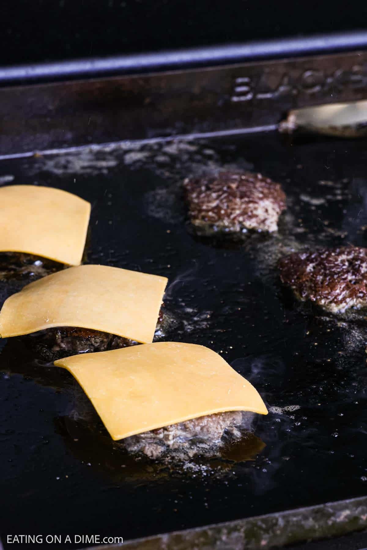 Slice cheese topped the cooked hamburger patties on the flat top griddle.