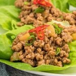 Ground chicken mixed with diced vegetables, topped with sliced red and green chili peppers, served in fresh lettuce leaves—these Asian ground chicken lettuce wraps bring vibrant flavor to your table on a crisp white plate.