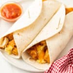 2 breakfast burritos on a white plate with a small side of salsa next to it.