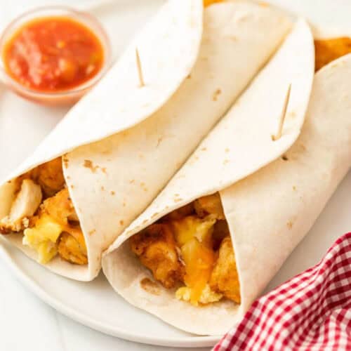 2 breakfast burritos on a white plate with a small side of salsa next to it.