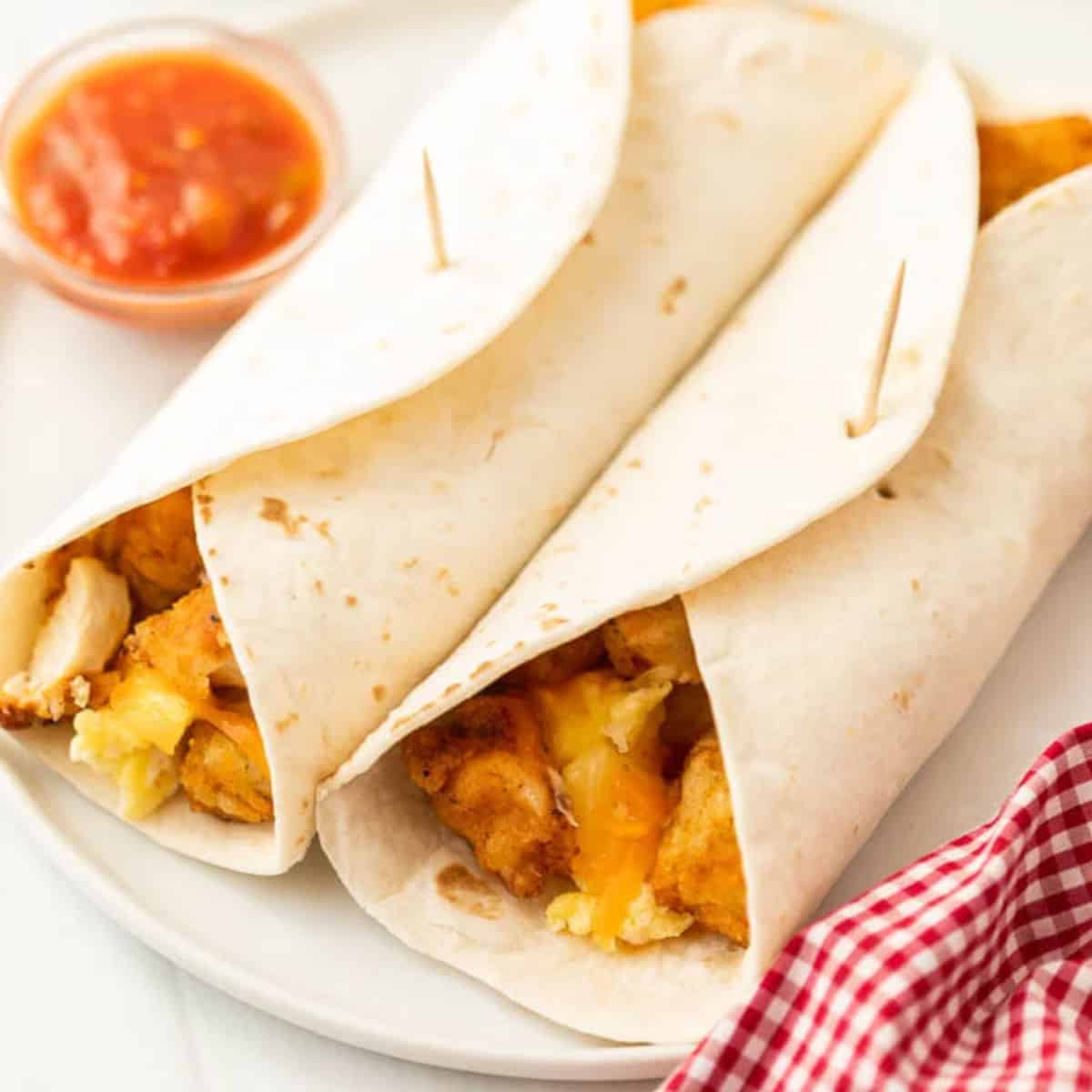 2 breakfast burritos on a white plate with a small side of salsa next to it.
