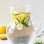 Cucumber lemon water in a pitcher with lemon slices.