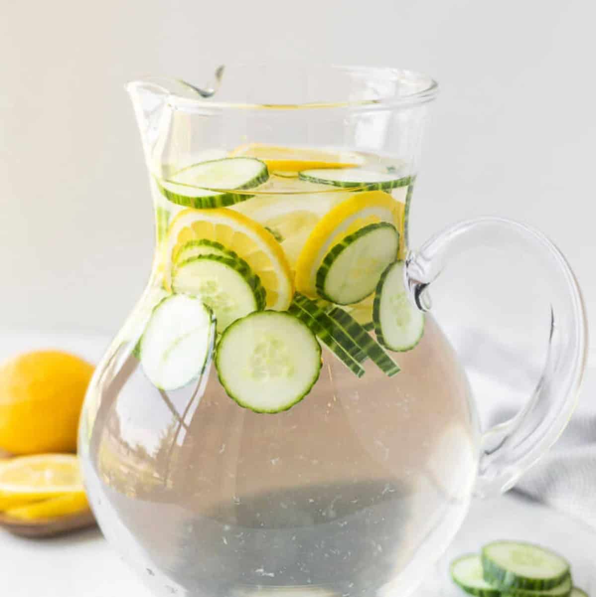 Cucumber lemon water in a pitcher with lemon slices.