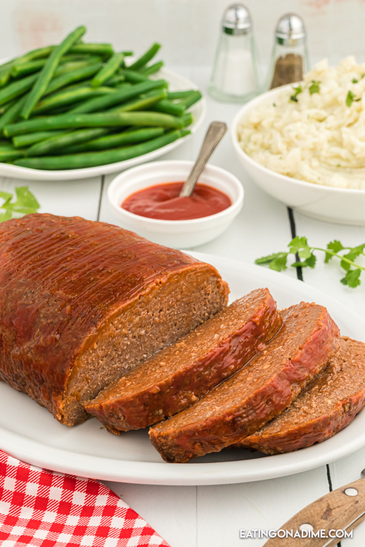 Meatloaf sliced on a white plate with a side of green beans and mashed potatoes