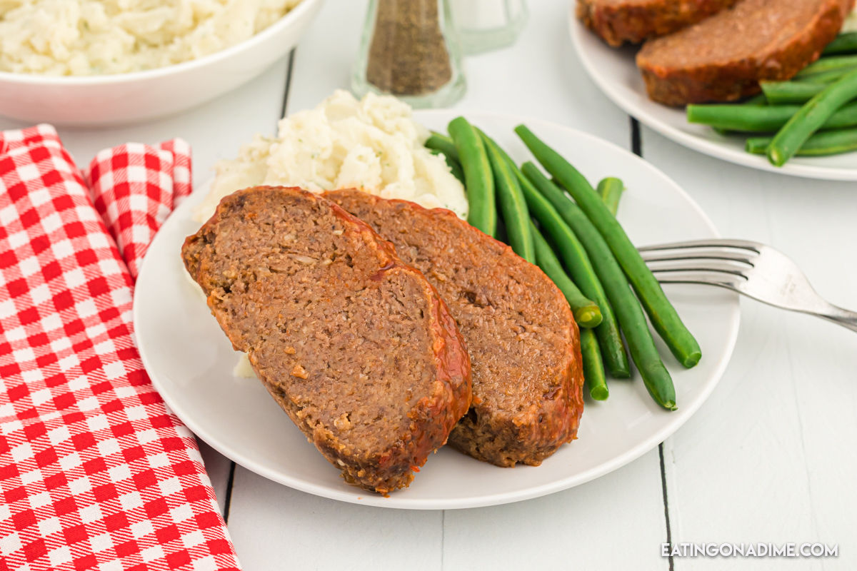 Meatloaf sliced on a white plate with a side of green beans and mashed potatoes