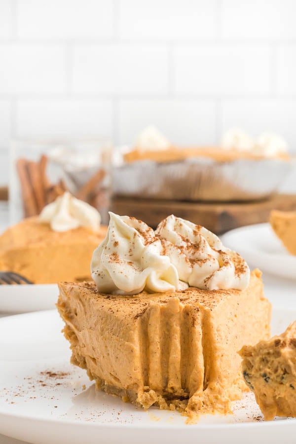 A slice of no bake pumpkin pie on a white plate with whipped topping