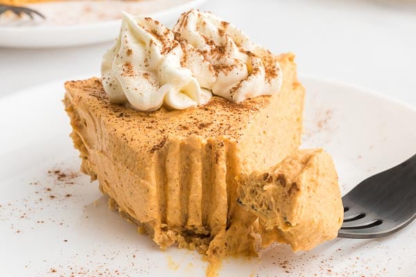A slice of no bake pumpkin pie on a white plate with whipped topping. With a bite on the fork