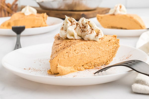 A slice of no bake pumpkin pie on a white plate with whipped topping