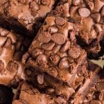 A close-up of several Starbucks Brownies topped with chocolate chips, with one brownie showing a bite taken out of it. The texture appears rich, fudgy, and slightly cracked on top.
