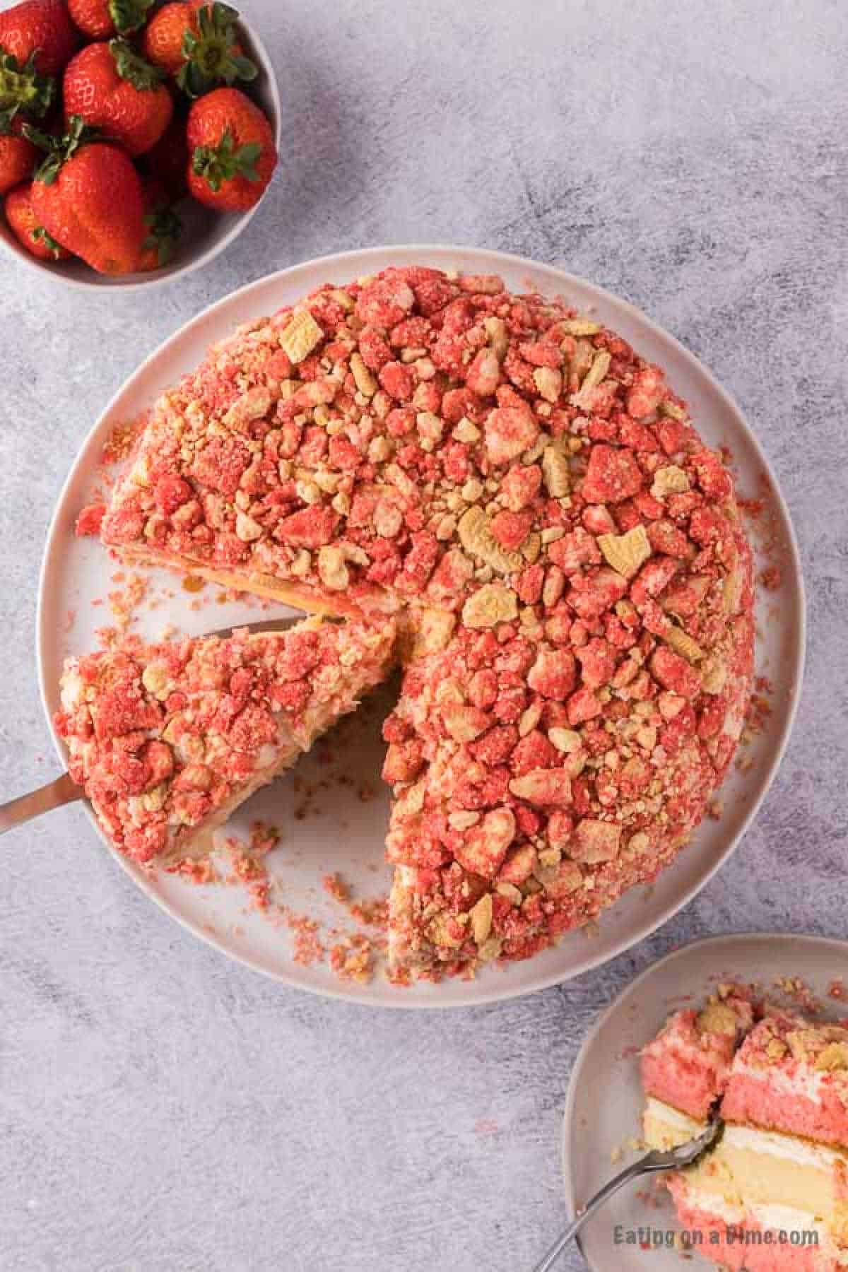 Close up image of strawberry shortcake cheesecake on a platter with a serving on a spatula.