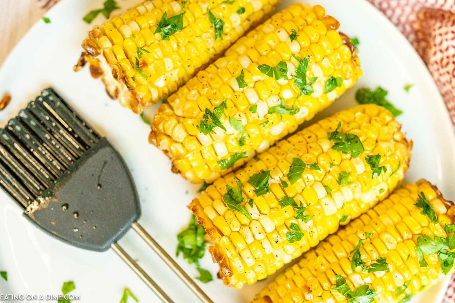 Air Fryer Corn on the Cob on a plate topped with cilantro with a spatula on the side. 