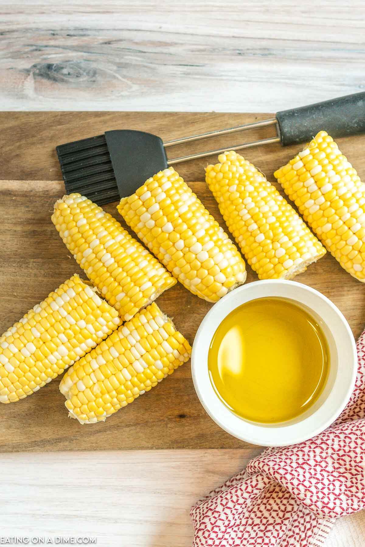 Corn on the cob on a platter with a melted butter on the side. 