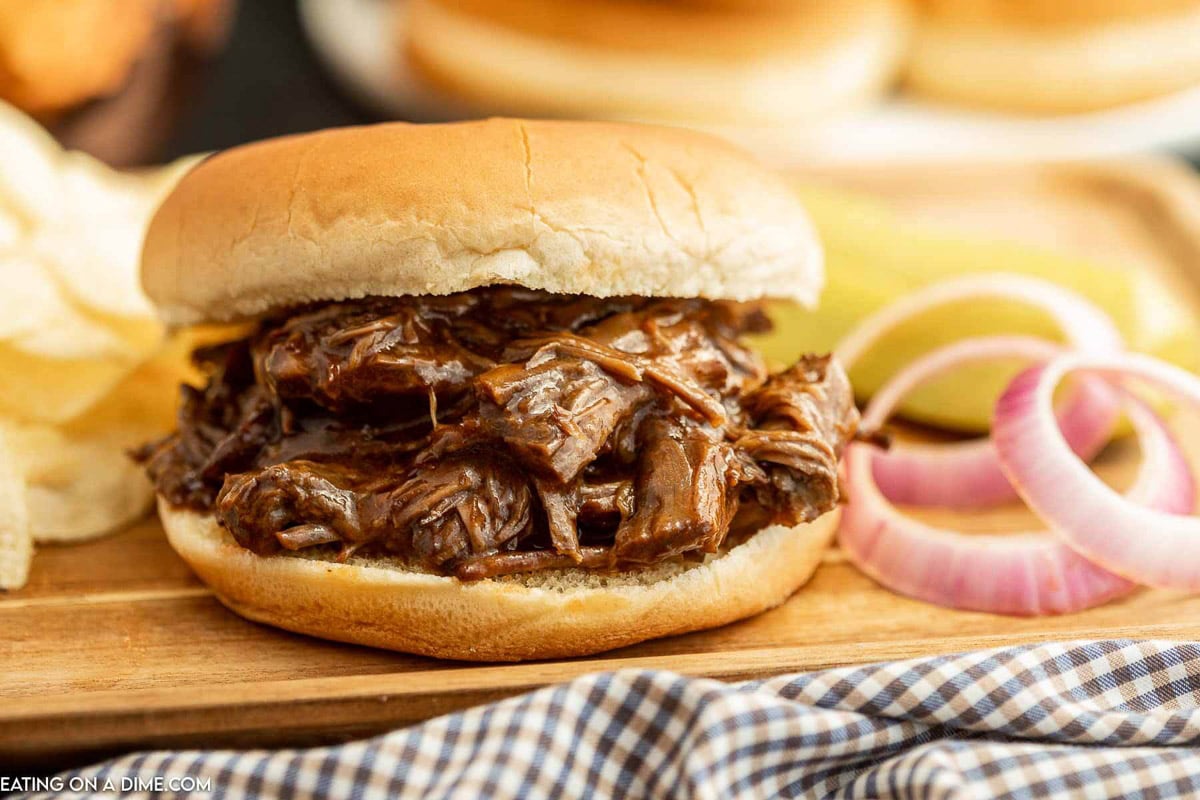 Shredded beef sandwich on a wooden platter with red onions on the side