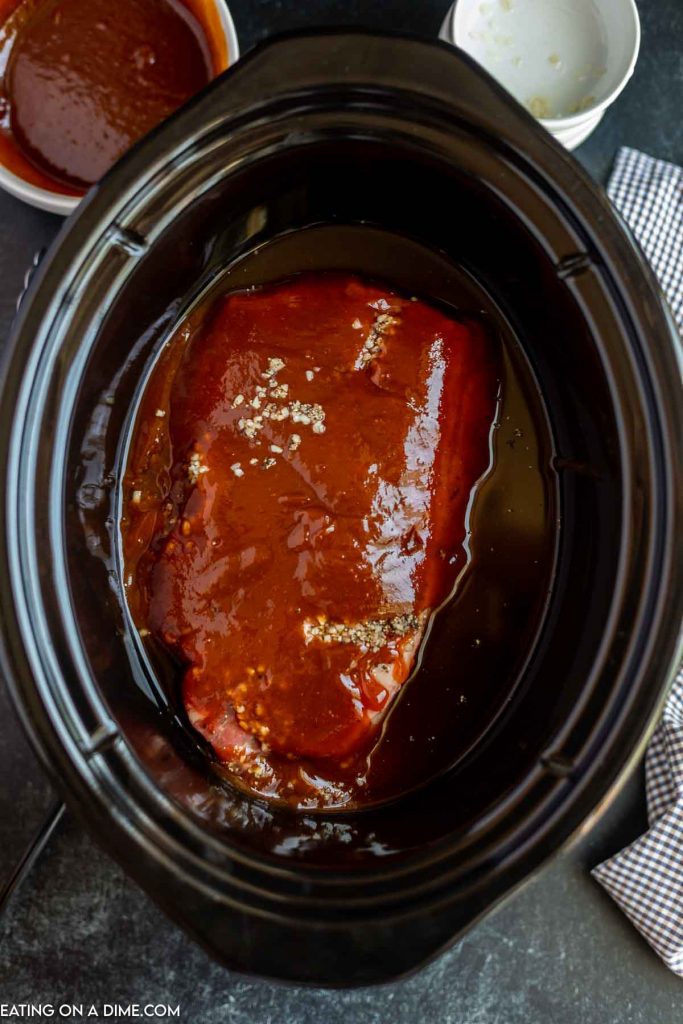 Uncooked beef in the crock pot topped with BBQ Sauce