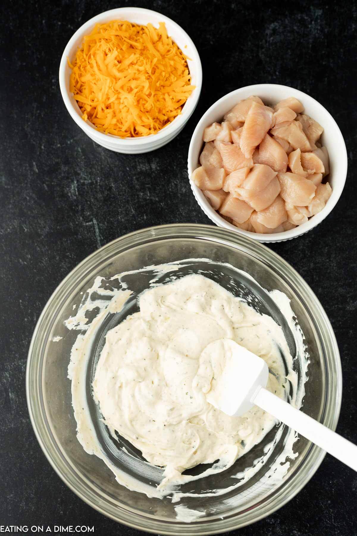 Mixing together the cream cheese, sour cream with a bowl of cheese and diced chicken on the side