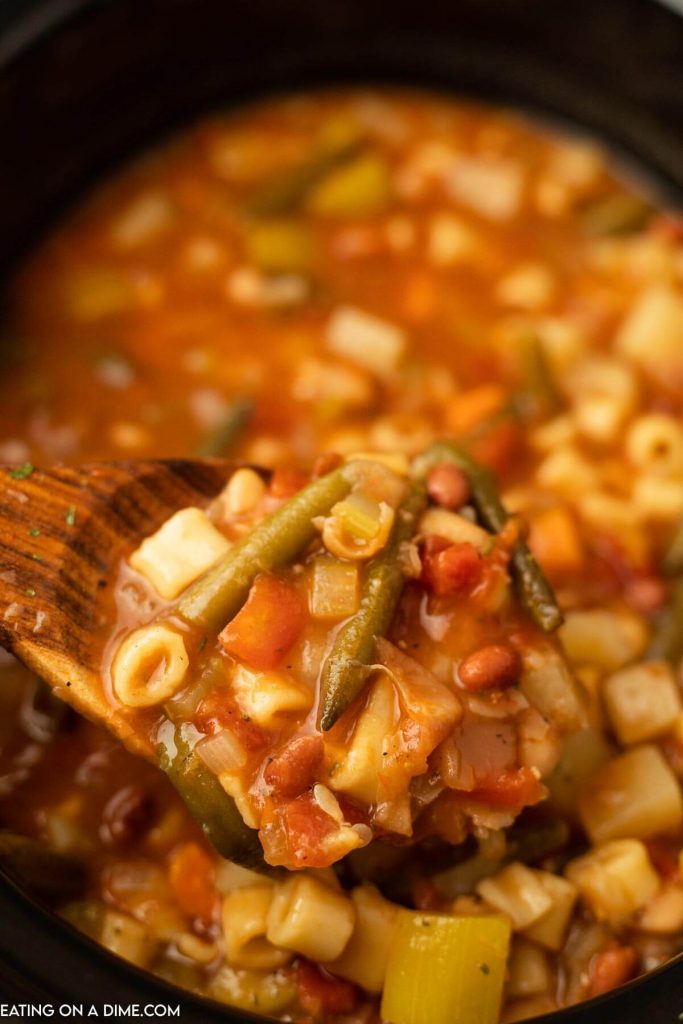 Minestrone Soup in a crock pot with a serving on a wooden spoon.