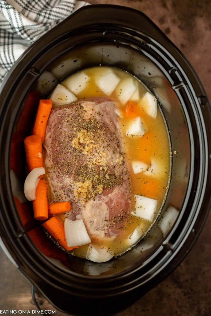 Uncooked pork roast in the crock pot with carrots and onions and gravy