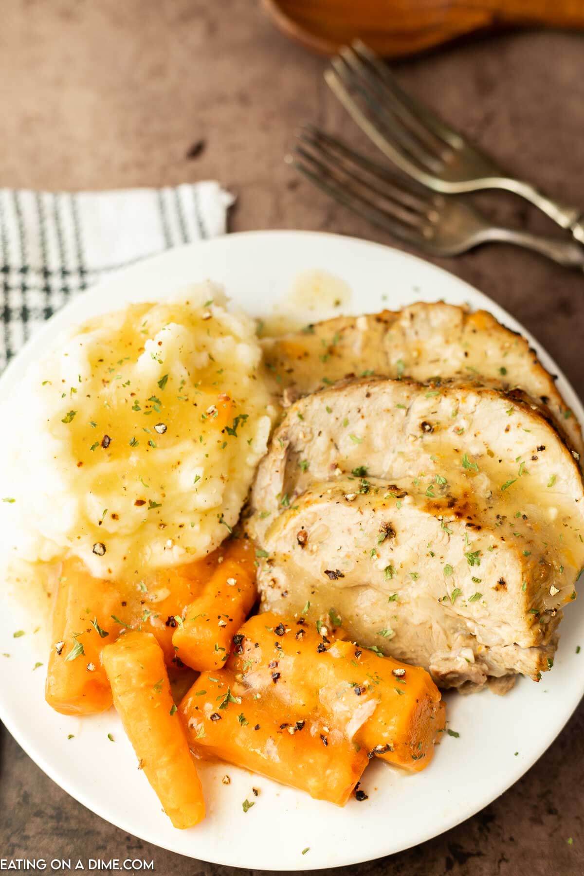 This Crock Pot Pork Roast is tender and delicious with very little work. The pork falls apart from being slow cooked and each bite is so flavorful. Pork Roast on a plate with a side of gravy and carrots drizzled with gravy