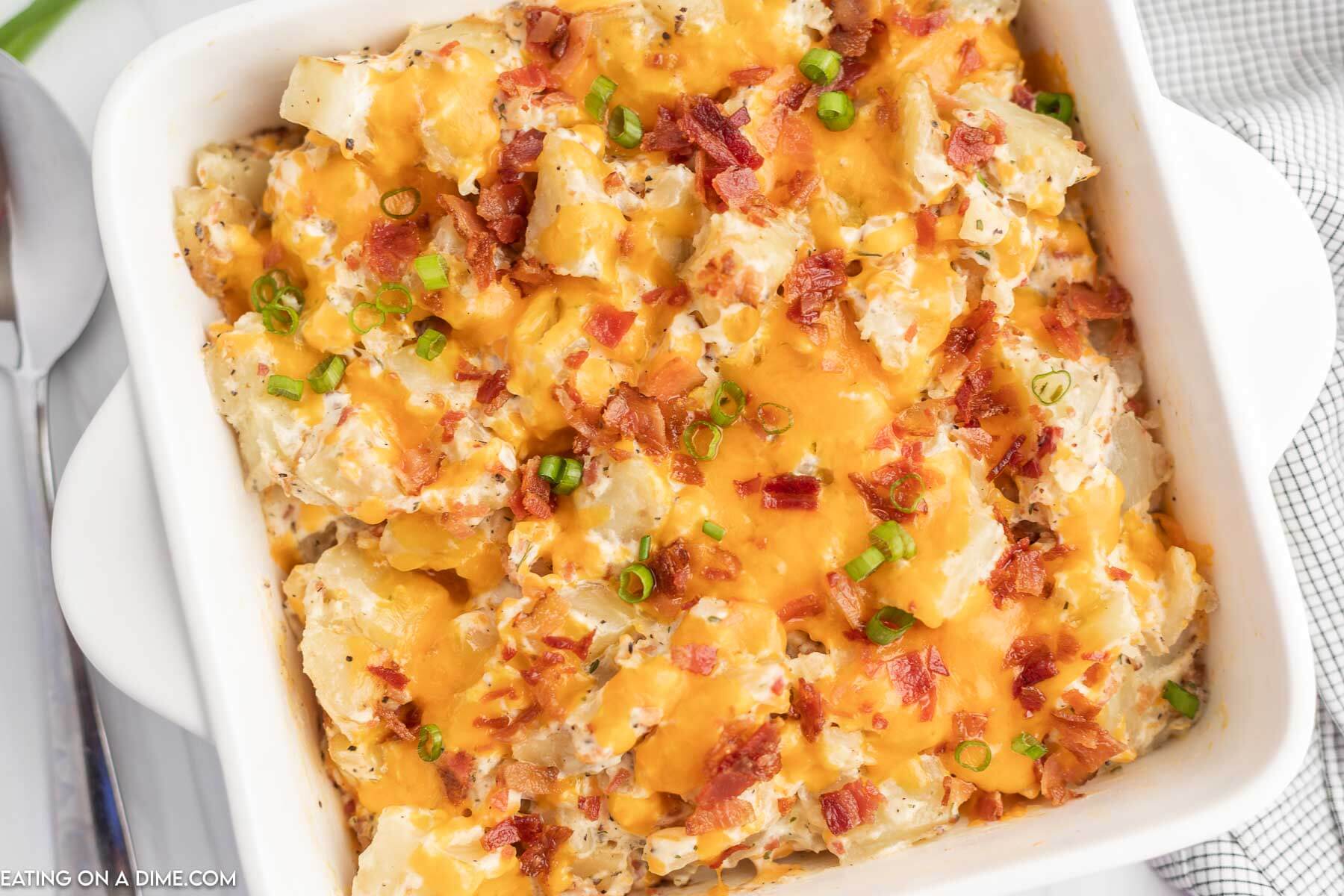 Crack Potatoes in a white casserole dish topped with melted cheese, chopped bacon and diced green onions