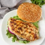 Grilled chicken on a white plate with lettuce and buns.