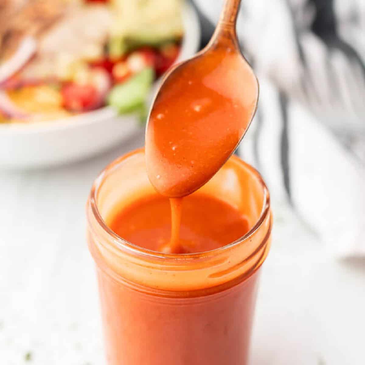Jar of orange colored dressing with a spoon.