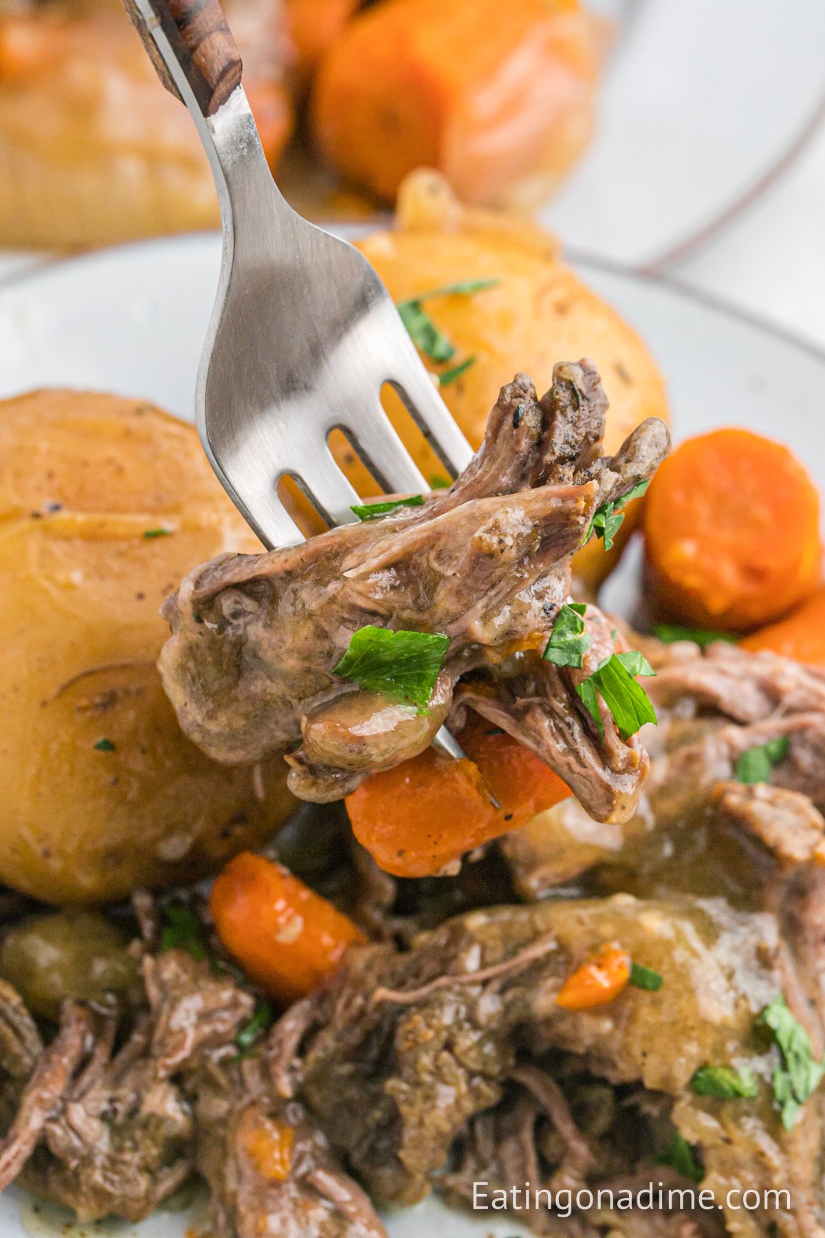 Chuck roast with potatoes and carrots on a platter with a serving on a fork