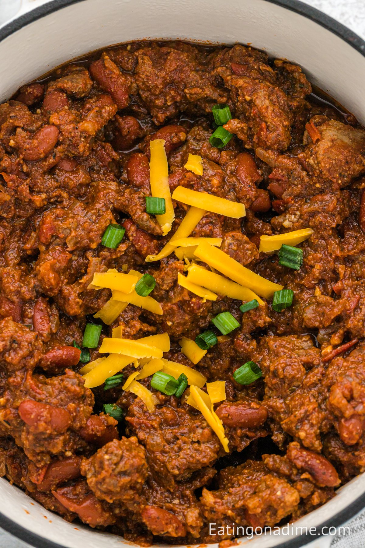 Chili in a dutch oven topped with cheese and green onions