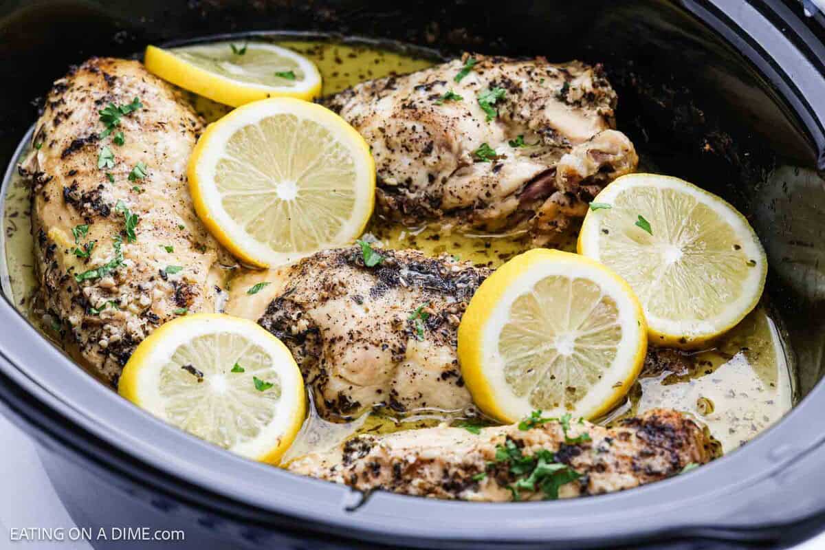 Chicken breasts cooked in a slow cooker with herbs, topped with fresh parsley and garnished with lemon slices in a light sauce—this Slow Cooker lemon garlic chicken recipe is flavorful and effortless.