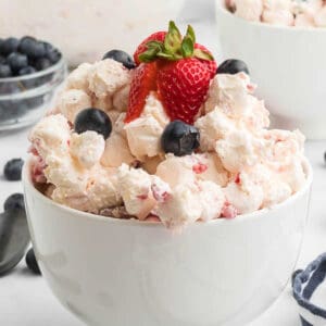 Cheesecake fruit salad topped with fresh berries in a bowl.