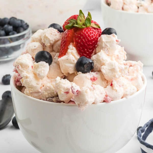 Cheesecake fruit salad topped with fresh berries in a bowl.