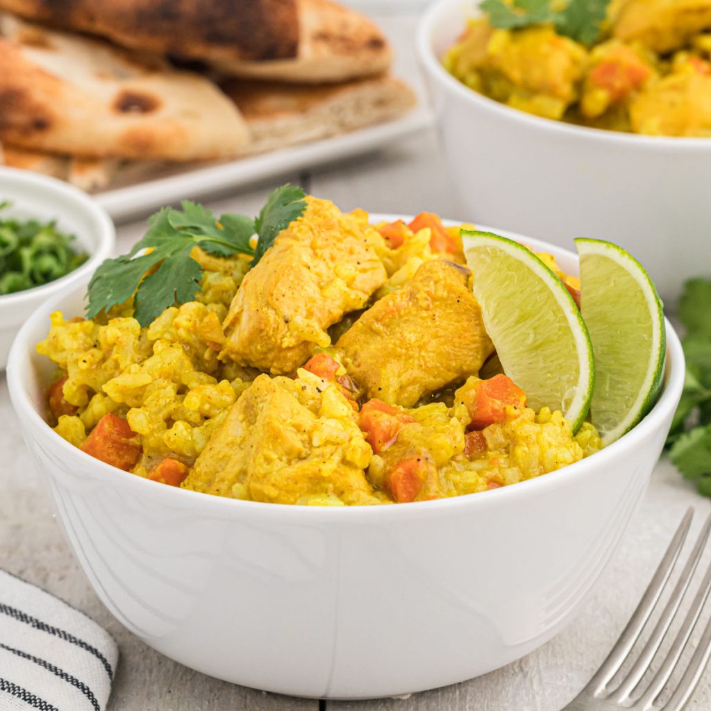 Close up image of chicken curry with rice and a lime in a white bowl. 