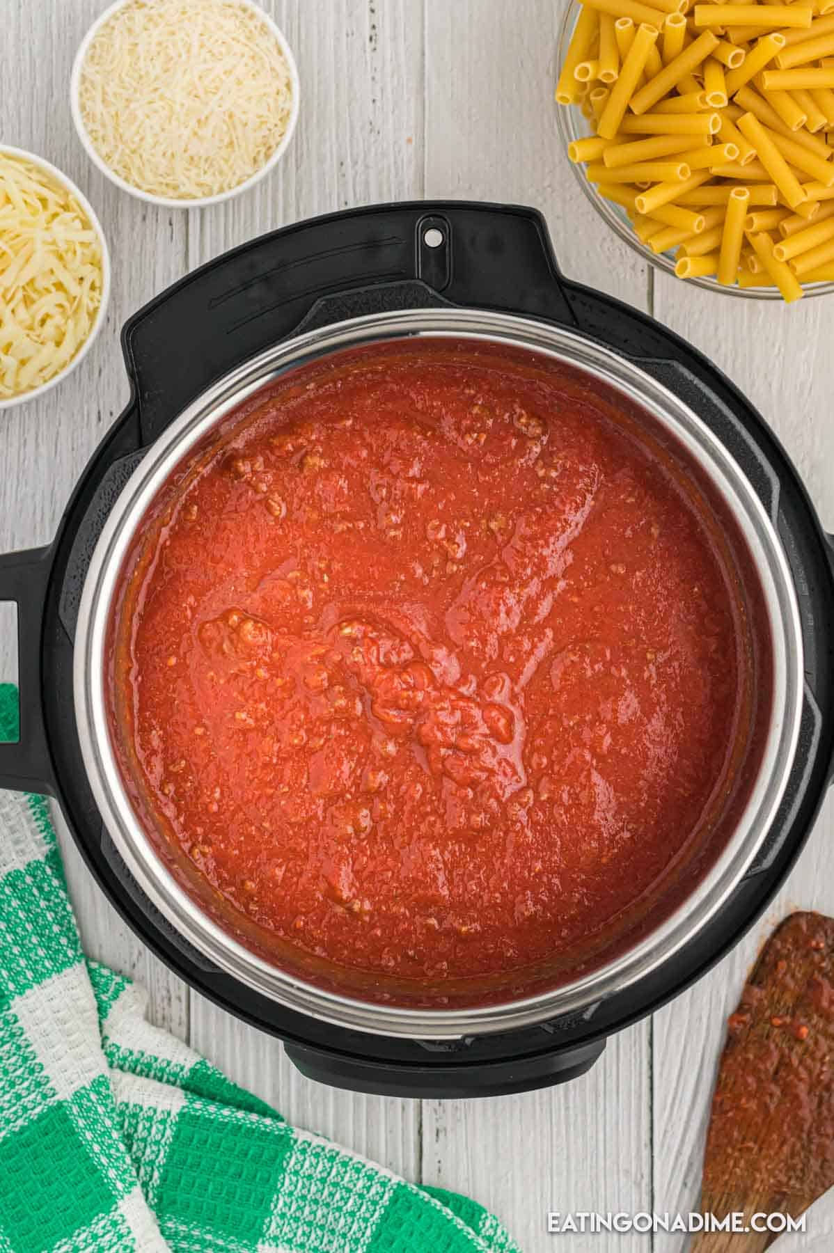 Crushed tomatoes poured into the instant pot with small bowls of shredded cheese and pasta on the side