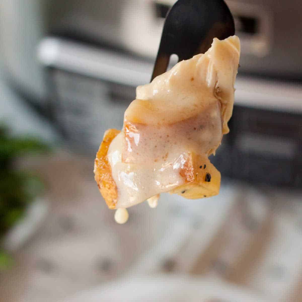 Close-up of a fork holding a piece of ravioli covered in creamy sauce, reminiscent of the rich flavors in a slow cooker lemon garlic chicken recipe. The filling reveals small chunks of mushrooms and herbs, set against a blurred background that hints at a cozy kitchen setting.
