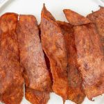 Crispy strips of vegan bacon made from a plant-based alternative are arranged side by side on a white plate, offering a great option for those seeking an air fryer turkey bacon substitute.