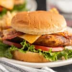 A Chick-fil-a Grilled Chicken Club sandwich with bacon, cheddar cheese, lettuce, and tomato on a toasted bun, served on a white plate.