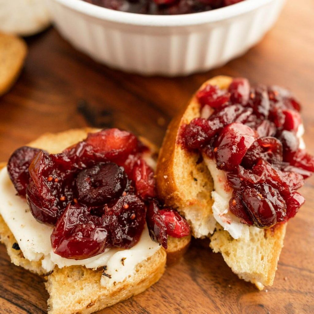 Cranberry Chutney on a slice of bread with cream cheese. A bowl of cranberry chutney in the background 