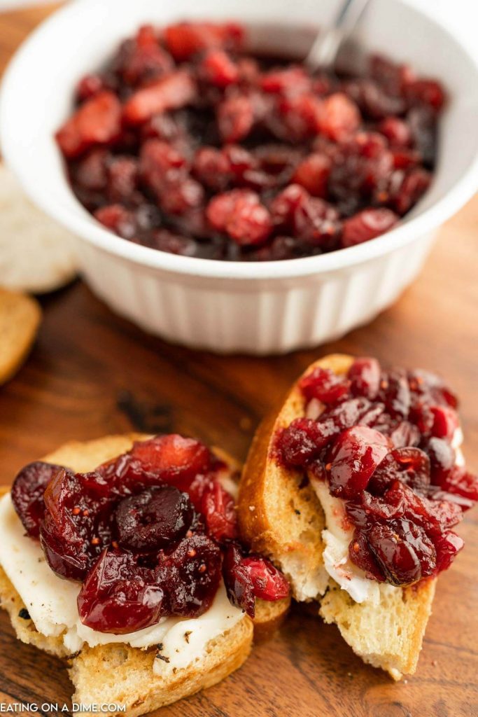 Cranberry Chutney on a slice of bread with cream cheese. A bowl of cranberry chutney in the background 